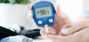 woman using a blood sugar testing device with a 98 mg/dl reading