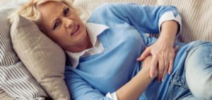 woman lying down on the couch holding her stomach in discomfort