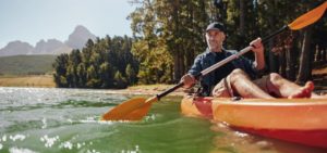 middle age man paddling a kayak down a river