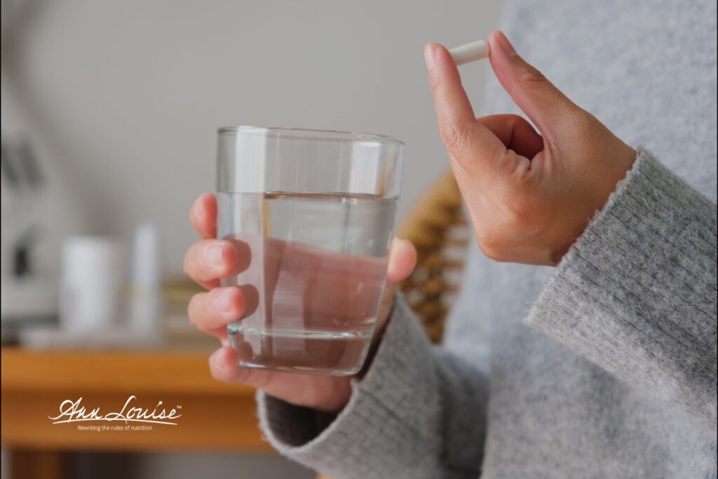 Woman taking a capsule of Para-Key, a natural parasite cleanse supplement, holding and 8 ounce glass of water.