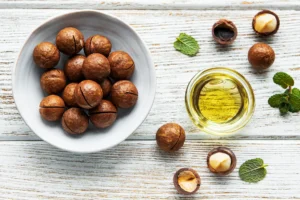 All natural macadamia nut oil in a bowl alongside several loose macadamia nuts on a weathered, whitewashed picnic table