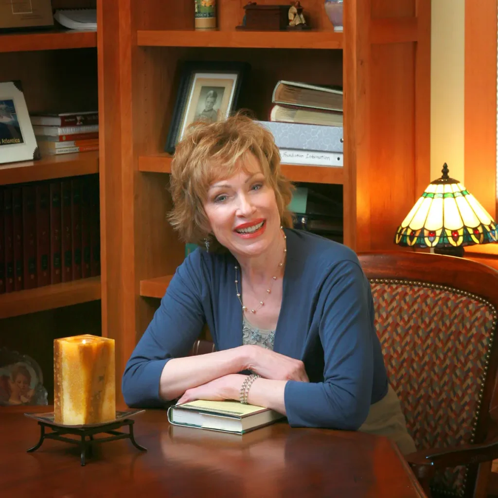Nutritionist and author Ann Louise Gittleman seated at her desk with a book in her wood-paneled home study